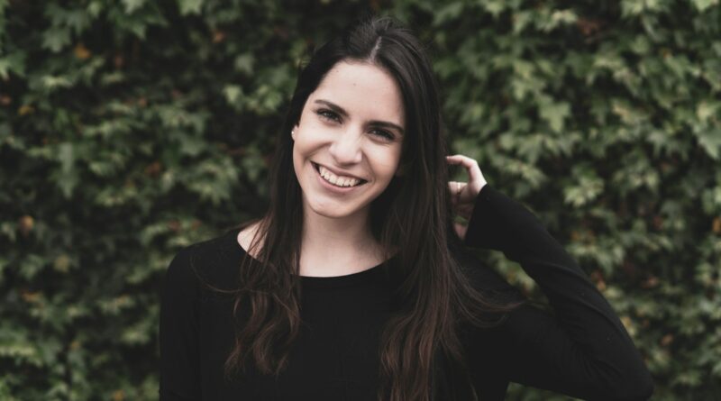 a smiling woman in a black top stands in front of a bush